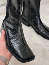 Bota negra de caña media con textura de cocodrilo, punta cuadrada y tacón bajo.