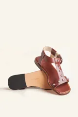 Sandalia de cuero color marrón con tiras finas, detalles de tachas metálicas y hebilla lateral.