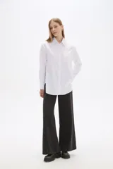 Camisa blanca de poliéster, corte holgado, con cuello camisero y cierre frontal con botones.