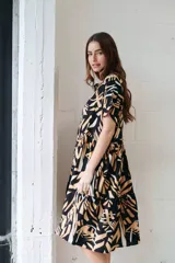 Vestido camisero midi con volados, estampado con hojas en tonos camel, blanco y negro. Tiene cuello redondo, mangas cortas y cierre frontal con botones.