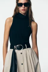 Vestido midi con falda beige con botones y cuerpo negro de cuello alto y sin mangas. Incluye cinturón negro con hebilla plateada.