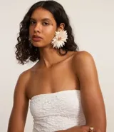 Vestido midi sin breteles confeccionado en encaje floral blanco. La prenda de escote recto viene justa hasta el cuadril donde comienzan los volados asimétricos.