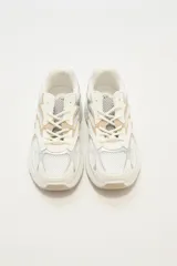Zapatillas deportivas blancas con detalles en plateado y beige, con cordones y suela gruesa.