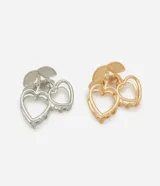 Kit de dos pinzas para el pelo tipo garra, con diseño de dos corazones huecos unidos por un tallo con hojas, simulando una cereza. Incluye una pinza en tono plateado y otra en tono dorado.