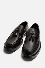 Mocasín de vestir color marrón oscuro, con detalle de borlas en la parte delantera, horma redonda y suela con ligero tacón.