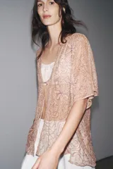 Blusa semitransparente color beige con bordados de hilo metalizado y abalorios. Tiene mangas cortas y cierre frontal con cordones.