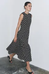 Vestido midi negro con estampado de lunares blancos, cuello redondo y sin mangas.