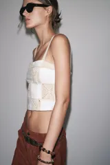Top blanco con diseño de crochet en beige, escote recto y tirantes finos.