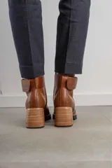 Bota corta de cuero marrón con puntera redondeada y taco cuadrado. Presenta una correa con hebilla alrededor del tobillo y cierre lateral.