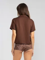 Camisa manga corta color marrón confeccionada en una mezcla de lino y tencel, con cuello camisero y cierre abotonado al frente.