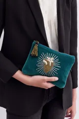 Bolso de mano tipo sobre, confeccionado en terciopelo color verde petróleo, con diseño de corazón bordado en canutillos y lentejuelas doradas y plateadas en el frente. Cuenta con cierre metálico superior y tirante de flecos de mostacillas doradas y negras.