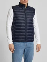 Chaleco acolchado azul marino de nailon reciclado, con cuello alto, cierre de cremallera, bolsillos laterales y logo de Tommy Hilfiger bordado en el pecho.
