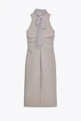 Vestido midi color gris topo, de cuello halter con lazada combinada a tono. Bajo con abertura en espalda. Cierre en espalda con cremallera, abertura y botón.