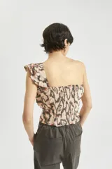 Top de algodón estampado con diseño abstracto en tonos beige, marrón y negro. Presenta un solo hombro y un volado grande que va desde el hombro hasta la cintura.
