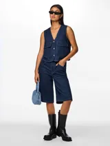 Chaleco denim azul oscuro, con cuello en V, cierre frontal con botones y bolsillos de parche.