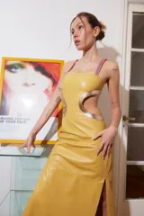 Vestido midi de cuero color maíz con cortes laterales y detalles dorados. Tiene tiras finas fucsias y abertura lateral en la falda.