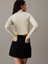 Top color crema de algodón con textura de canalé, corte slim, largo cropped, cuello alto y manga larga.