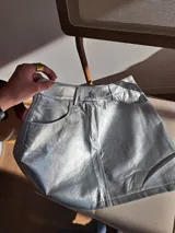 Minifalda plateada de cuero sintético con bolsillos delanteros y cierre con botón.