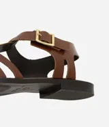 Sandalias planas de cuero marrón con tiras entretejidas, hebilla dorada y suela negra.