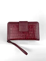 Billetera tipo clutch o cartera de mano, color vino tinto, con textura de cuero cocodrilo (crocco). Presenta un cierre de solapa con broche y costuras en contraste color claro. Incluye una correa de muñeca desmontable.