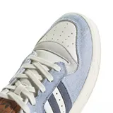 Zapatillas urbanas Adidas Rivalry Low, color blanco con detalles en celeste y azul marino. Confeccionadas en cuero y gamuza, con las tres tiras características de la marca en los laterales.