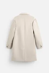 Abrigo recto color beige confeccionado en tejido con lana. Tiene cuello con solapas de muesca, manga larga con puños abotonados, bolsillos de vivo en la cadera, bolsillo interior, abertura en el centro de la espalda y cierre frontal con botonadura.