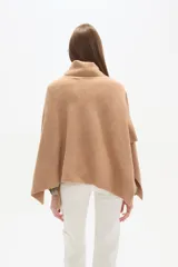 Poncho tejido color tostado, con cuello alto tipo tortuga y diseño asimétrico en el ruedo.