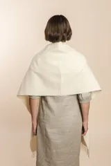 Chal beige con bolsillos de cuero y terminaciones en flecos, diseñado para un ajuste cómodo en los hombros.