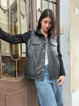 Campera negra con cuerpo de cuero y mangas de lana. Tiene corte recto, cuello camisero, cierre frontal con botones dorados, dos bolsillos con solapa en el pecho y detalles de tachas doradas.