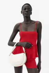 Bolso de hombro ovalado color crema con asa de doble tira redonda con detalles metalizados dorados. Incluye cierre imantado, asa de bandolera extraíble con tejido a contraste y bolso interior con cierre mediante cremallera metálica.