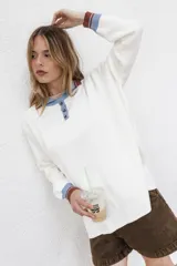 Buzo blanco de algodón con cuello polo con botones, mangas largas con puños acanalados a rayas en tonos marrón y celeste.