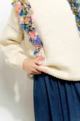Sweater color crema de tejido de punto con cuello redondo y mangas largas. Presenta flecos de colores en los hombros.