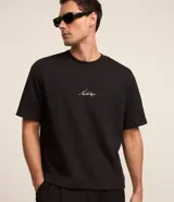 Remera negra de corte boxy con cuello redondo y manga corta. Presenta una estampa con la palabra "Nostalgia" en el centro del pecho.