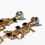 Aros colgantes dorados con dije superior de cristal facetado y colgantes de ramas doradas y cuentas negras.