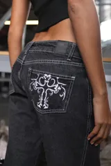 Pantalón denim straight color negro con lavado efecto crudo, acceso con cierre metálico y botón, cinco pasacintos, bolsillos laterales y traseros con bordado.