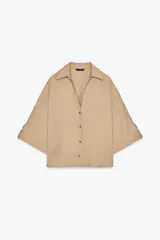 Camisa color beige de cuello solapa con escote pico y manga corta ancha acabada en vuelta con trabilla y botón. Cierre frontal con botones.
