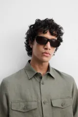 Sobrecamisa verde militar de lino, corte relaxed fit, con cuello solapa, manga larga con puños abotonados, bolsillos de parche con solapa en el pecho, aberturas laterales en el bajo y cierre frontal abotonado.