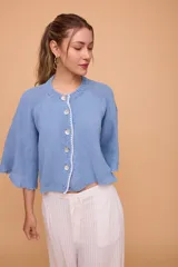 Saco tejido a máquina en lino y algodón color celeste, con silueta en línea A, mangas anchas, escote redondo con bordado en la delantera y botones de nácar. Largo por arriba de la cola.