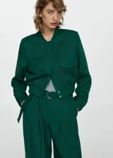 Chaqueta bomber verde esmeralda de lino y lyocell, con cuello redondo, cierre frontal con botones a presión, cintura y puños elásticos, dos bolsillos de parche con solapa en el pecho y corte cropped.