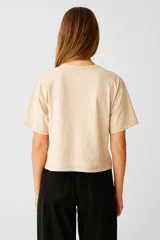 Remera corta color crudo de algodón, con cuello redondo y mangas cortas. Presenta tres lazos bordados en el frente.