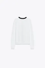 Chaqueta blanca de punto con cuello redondo y manga larga. Tiene falsos bolsillos de vivo en el delantero y cierre frontal con botones dorados.