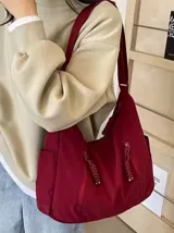 Bolso hobo color bordó de tela suave, liviana y espaciosa, con bolsillos frontales con cierre y correa ajustable.