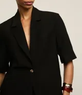 Blazer negro de viscosa con mangas cortas, solapas en el cuello y botón metalizado.