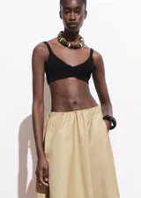 Falda larga color beige, de tiro bajo y corte evasé, con cintura elástica y bolsillos laterales.