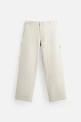Pantalón de denim color beige, corte relaxed fit, con cinco bolsillos, efecto lavado, aplicación de tira y bolsillo multifunción en perneras. Cierre frontal con cremallera y botón.
