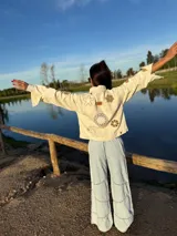 Campera de jean color manteca con apliques de flores de crochet en tonos neutros, corte recto y cierre con botones.