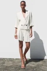 Blazer blanca de cuello solapa y manga corta con vuelta. Bolsillos delanteros de vivo y cierre frontal cruzado con botones.