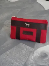 Sobre tipo cartuchera color borgoña, de lona con terminaciones en cuero marrón. Tiene cierre superior y aplique de cuero con el logo de la marca.