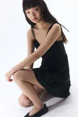 Vestido corto negro de popelina de algodón con breteles finos ajustables con moña, escote corazón y cuerpo entallado con costuras decorativas y espalda fruncida. Falda acampanada con costura fruncida en el bajo.