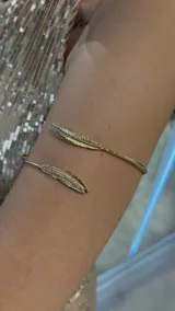 Brazalete dorado abierto con apliques de plumas en los extremos.